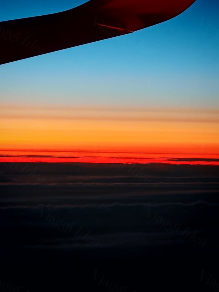 Vista dal finestrino dell'aereo sopra le nuvole con una striscia arancione all'orizzonte