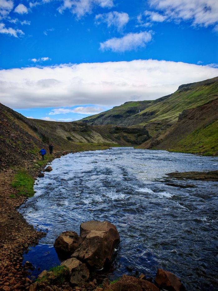 Due persone camminano lungo la riva di un fiume fra colline verdi