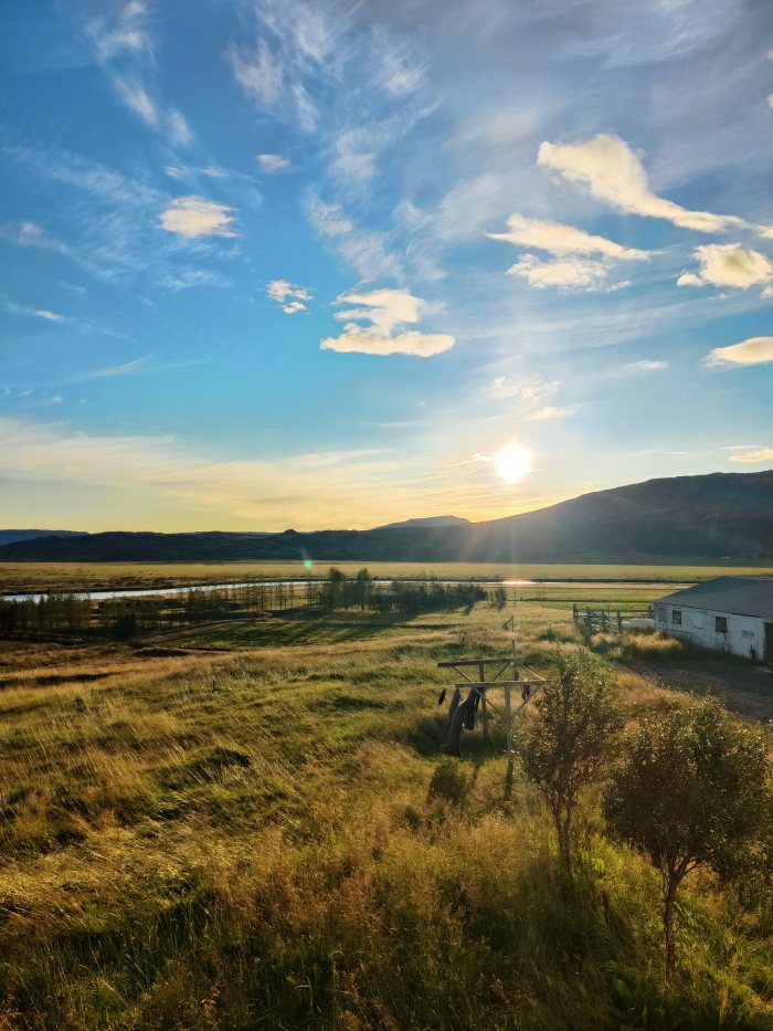 Campo erboso con fiume e capanno di legno alla luce bassa del sole