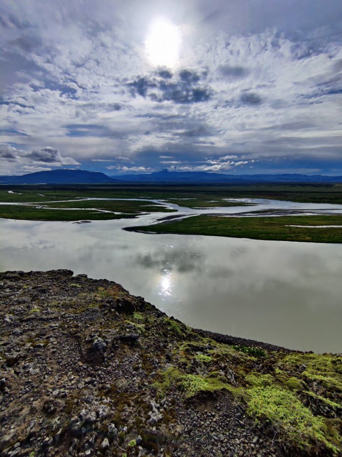 Fiume che serpeggia fra pianure verdi e montagne lontane