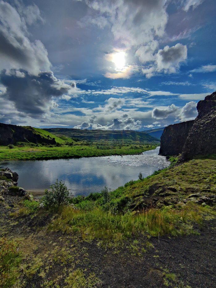 Fiume che scorre fra colline e rocce sotto un cielo nuvoloso