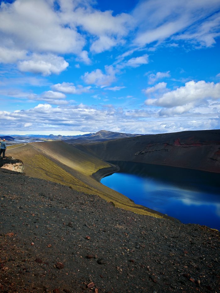 Una persona osserva un lago blu dentro un cratere vulcanico