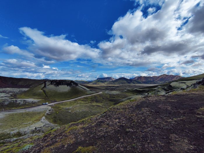 Un'auto su una strada in un paesaggio montuoso con cielo nuvoloso