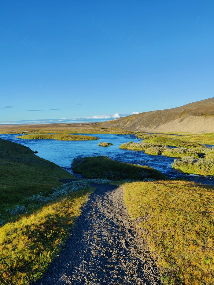 Sentiero di ghiaia che scende verso un fiume con la luce bassa
