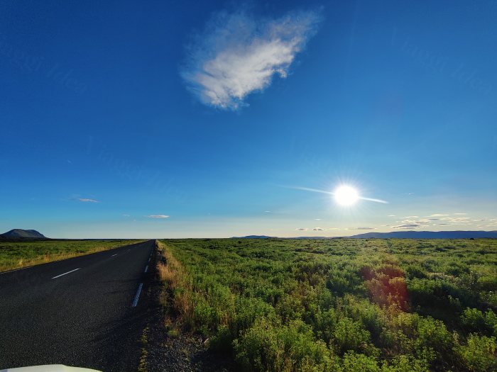 Strada asfaltata che attraversa un paesaggio aperto con il sole basso