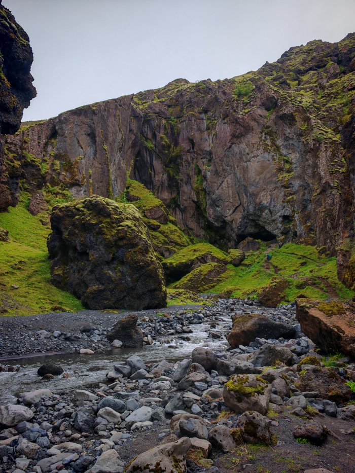 Escursionista cammina lungo un sentiero fra rocce e un torrente