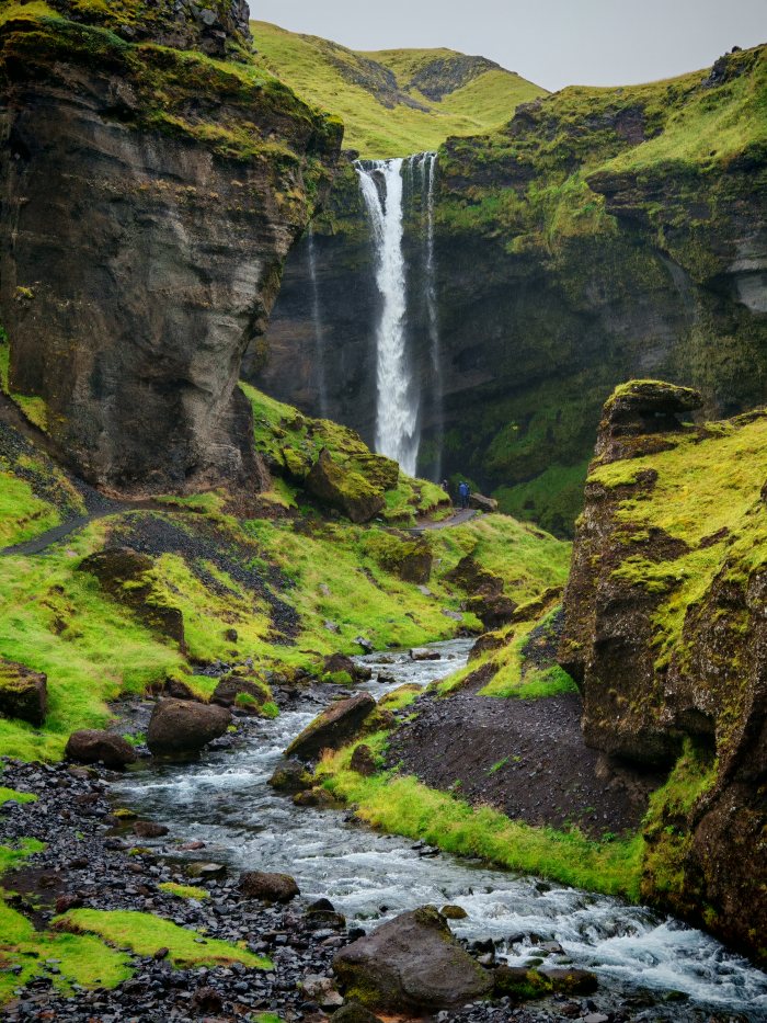 Due persone davanti a un grande salto d'acqua fra rocce coperte di muschio
