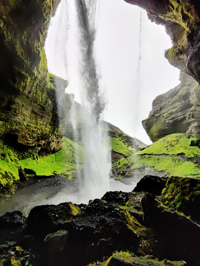Cascata che cade dentro una gola verde, vista da dietro il getto