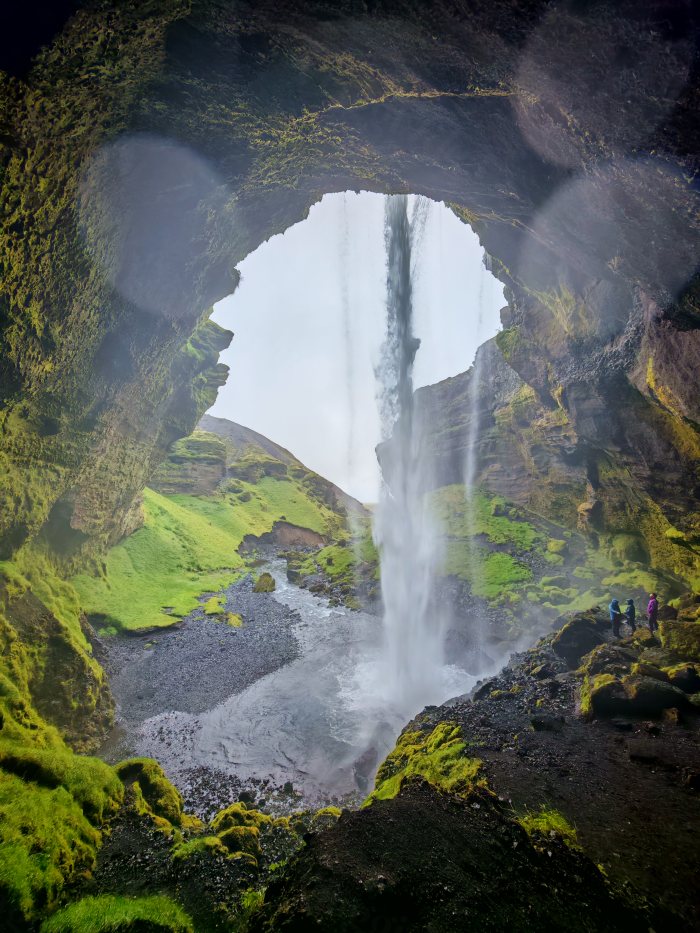 Cascata vista attraverso un arco naturale di roccia coperto di muschio