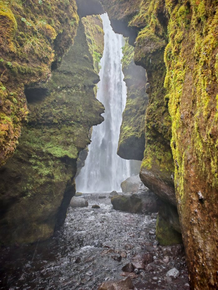 Acqua che cade da una stretta fenditura fra rocce coperte di muschio