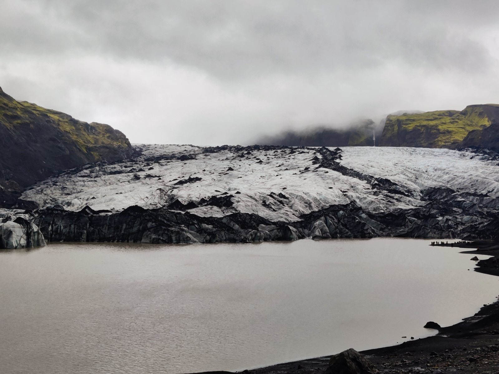 Gruppo di persone osserva un grande ghiacciaio con lago in primo piano