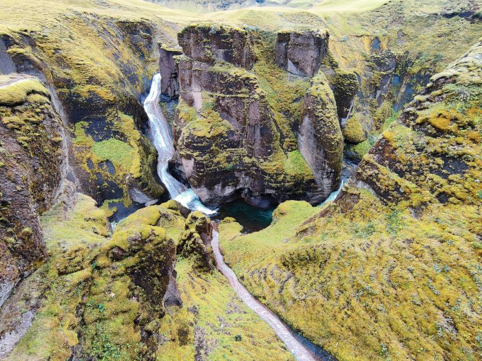 Canyon con cascata e fiume fra rocce ricoperte di muschio