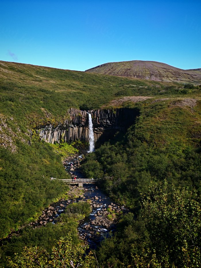 Un visitatore attraversa un ponte sopra un fiume vicino a una cascata