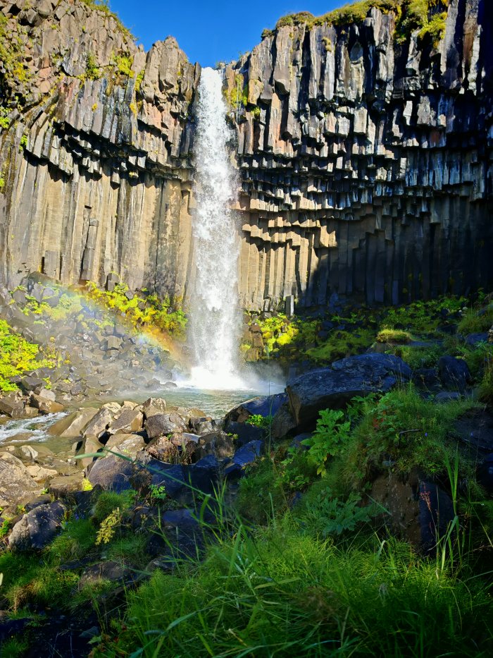 Acqua che cade da alte pareti di colonne basaltiche con vegetazione verde