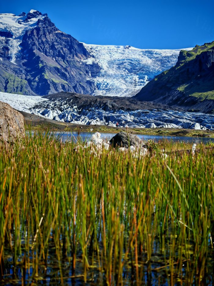 Due escursionisti si avvicinano a un lago con il ghiacciaio in lontananza