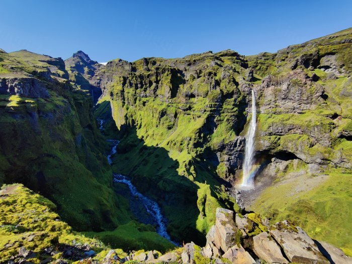 Cascata che cade in un canyon con vegetazione verde e cielo azzurro
