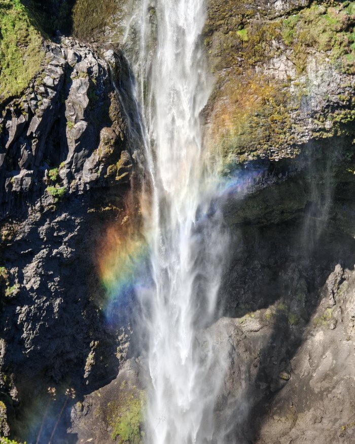 Acqua che cade da una scogliera formando un arcobaleno fra le rocce