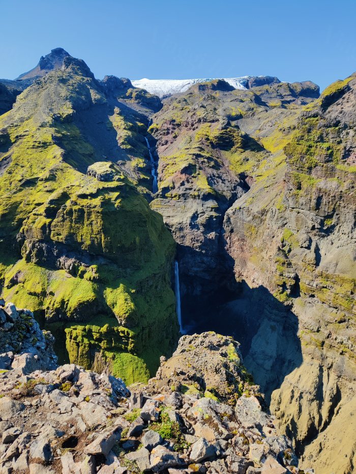 Cascata che scende fra monti coperti di muschio con ghiacciaio sullo sfondo