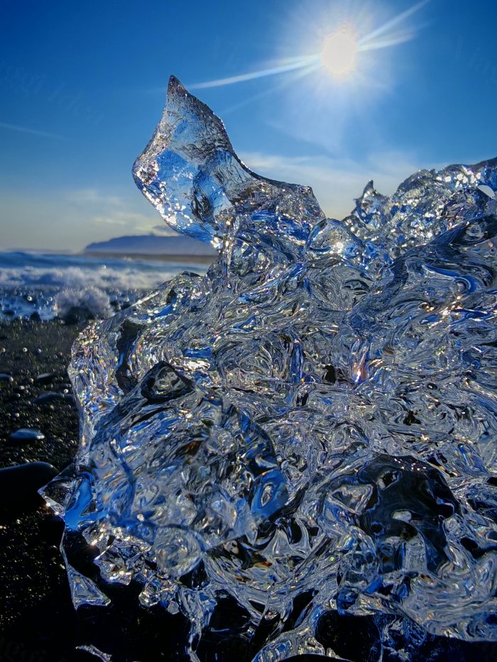Ghiaccio trasparente su una spiaggia nera con onde e il sole in alto