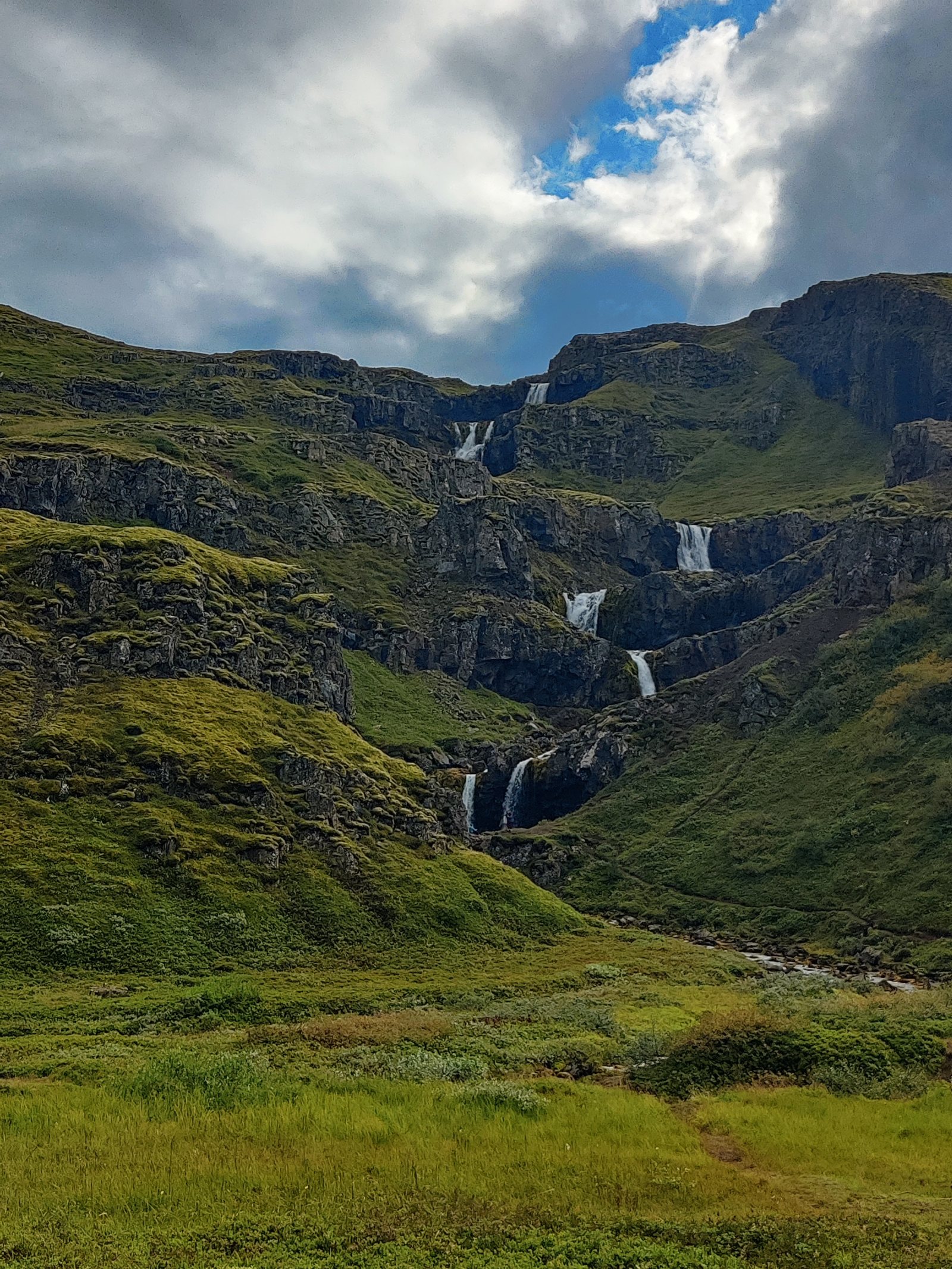 Cascata in un canyon montuoso con vegetazione verde e cielo nuvoloso