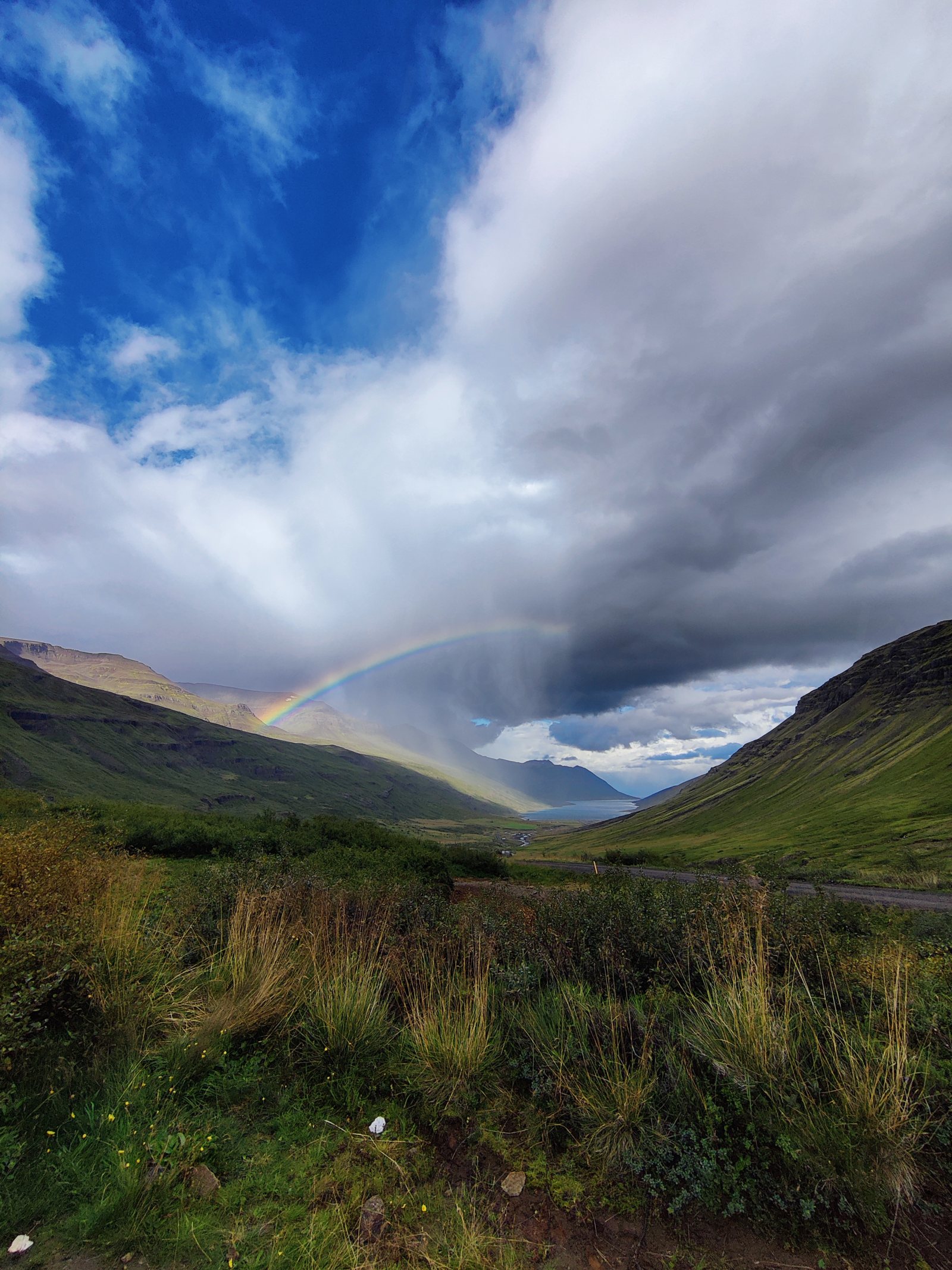 Arcobaleno sopra una valle con montagne e una strada