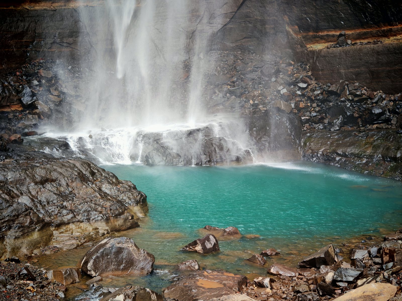 Acqua che cade da una scogliera in un lago turchese circondato da rocce