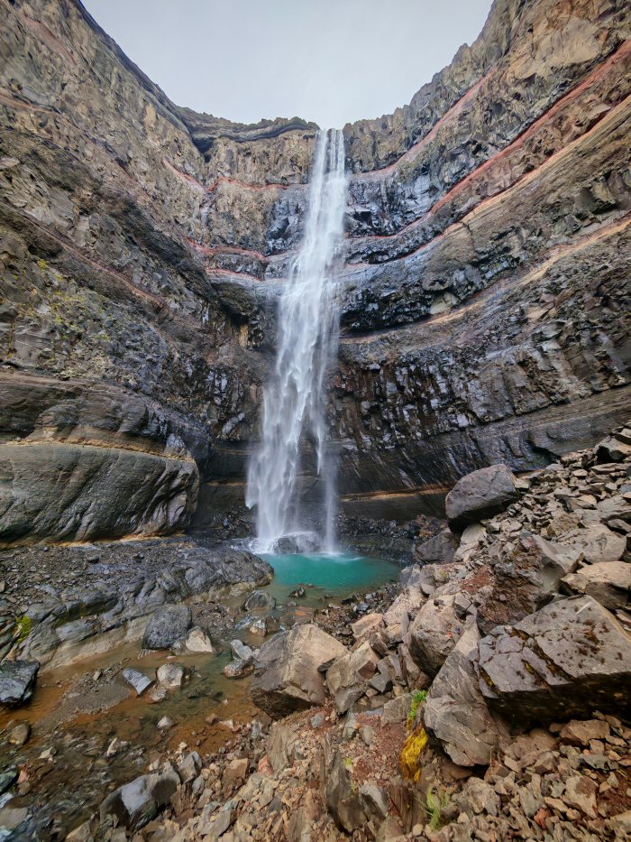 Cascata che cade in una pozza turchese fra rocce stratificate
