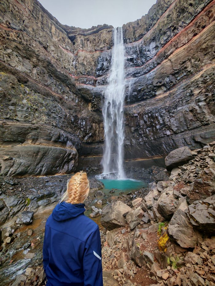 Una persona osserva una cascata che cade in un bacino turchese