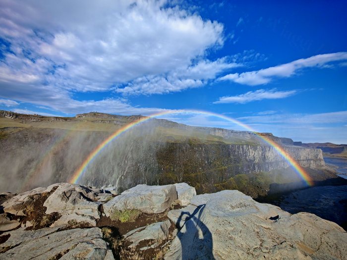 Un fotografo cattura un arcobaleno sopra la cascata, con la sua ombra sulle rocce