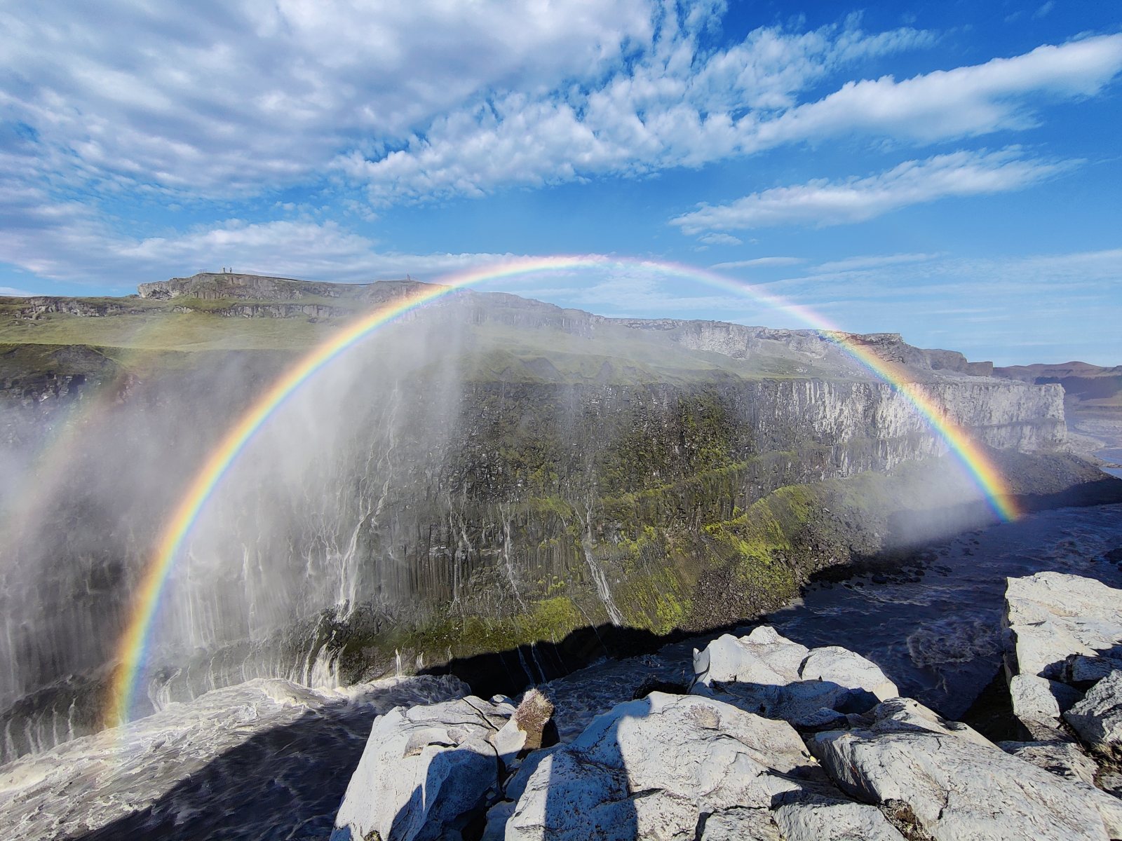 Arcobaleno sopra una cascata con acqua che cade da un dirupo roccioso
