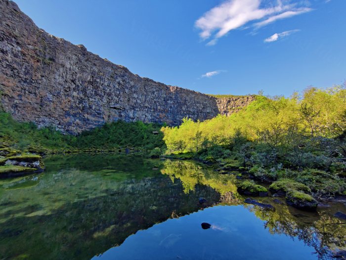 Lago che riflette pareti rocciose e vegetazione verde
