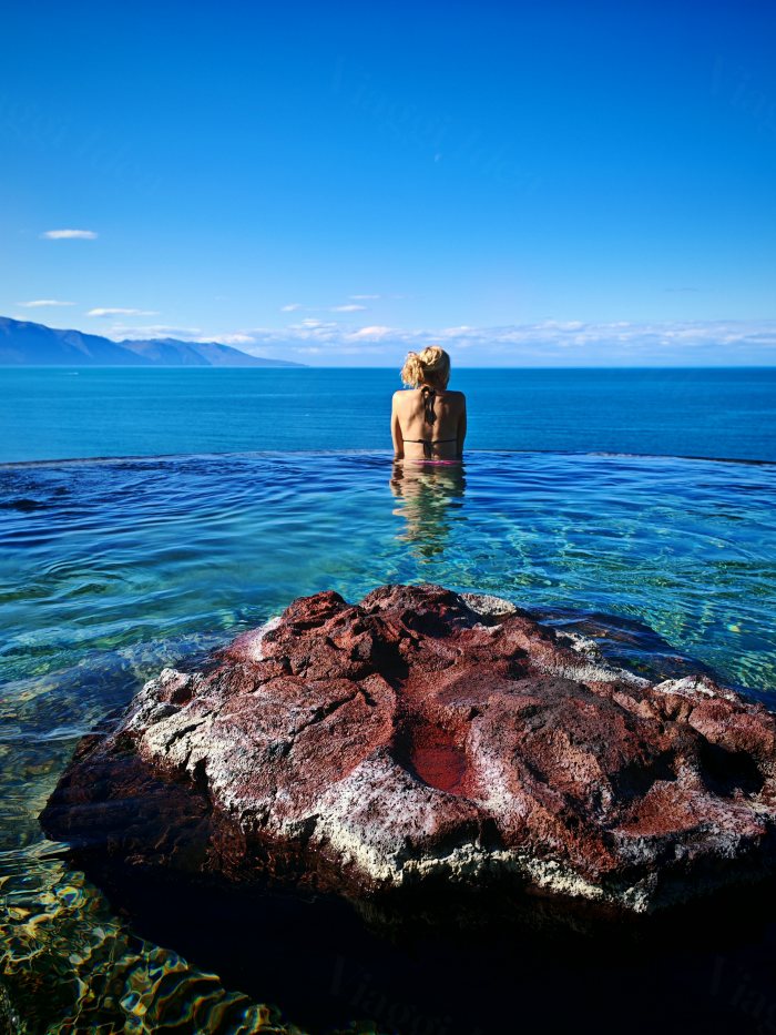Persona in una piscina a sfioro con vista sul mare e le montagne