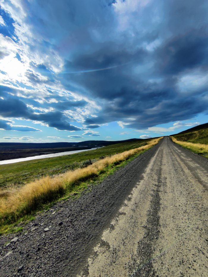 Strada sterrata che si estende verso l'orizzonte con fiume e cielo nuvoloso