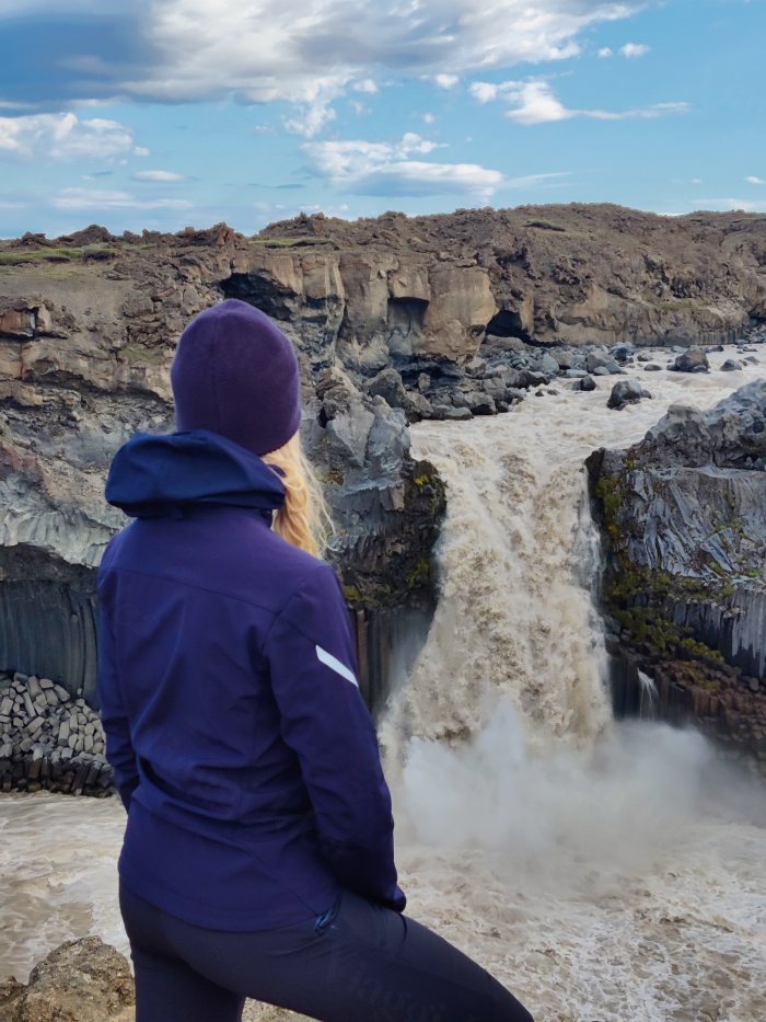 Una donna osserva un imponente salto d'acqua in un paesaggio vulcanico