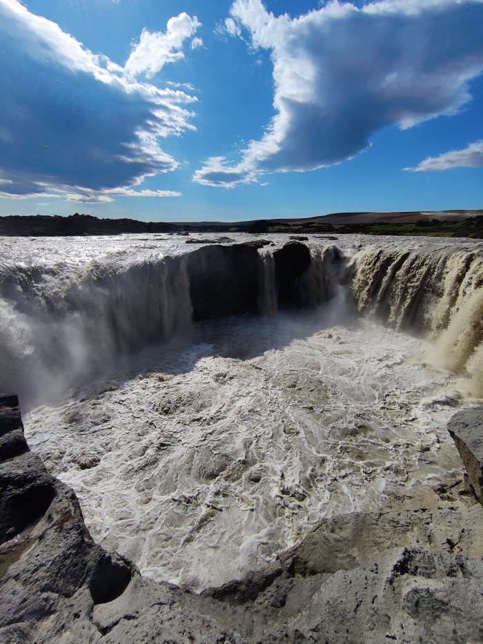 Acqua che cade da un precipizio in un paesaggio roccioso sotto cielo nuvoloso