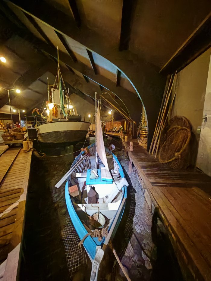 Navi da pesca esposte in un magazzino con passerelle di legno