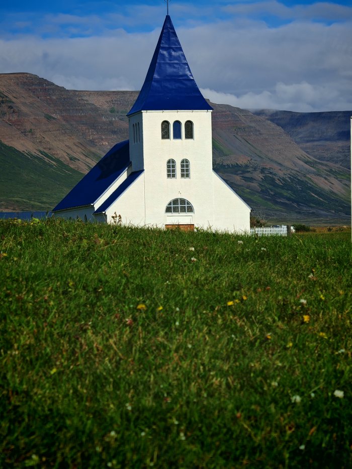 Chiesa bianca con tetto blu in un campo verde con montagne