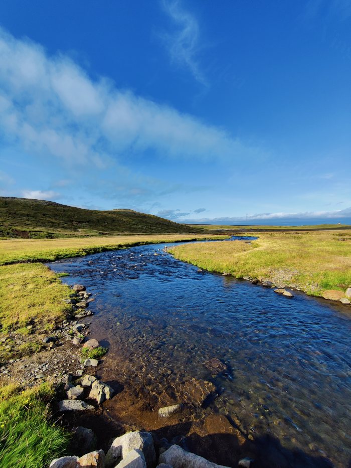 Fiume che scorre fra campi erbosi e colline sotto cielo azzurro