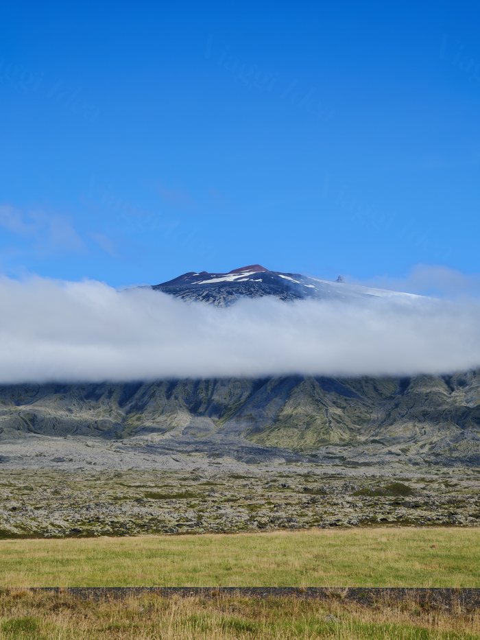 Montagna con cima innevata circondata da nuvole vista da un campo erboso