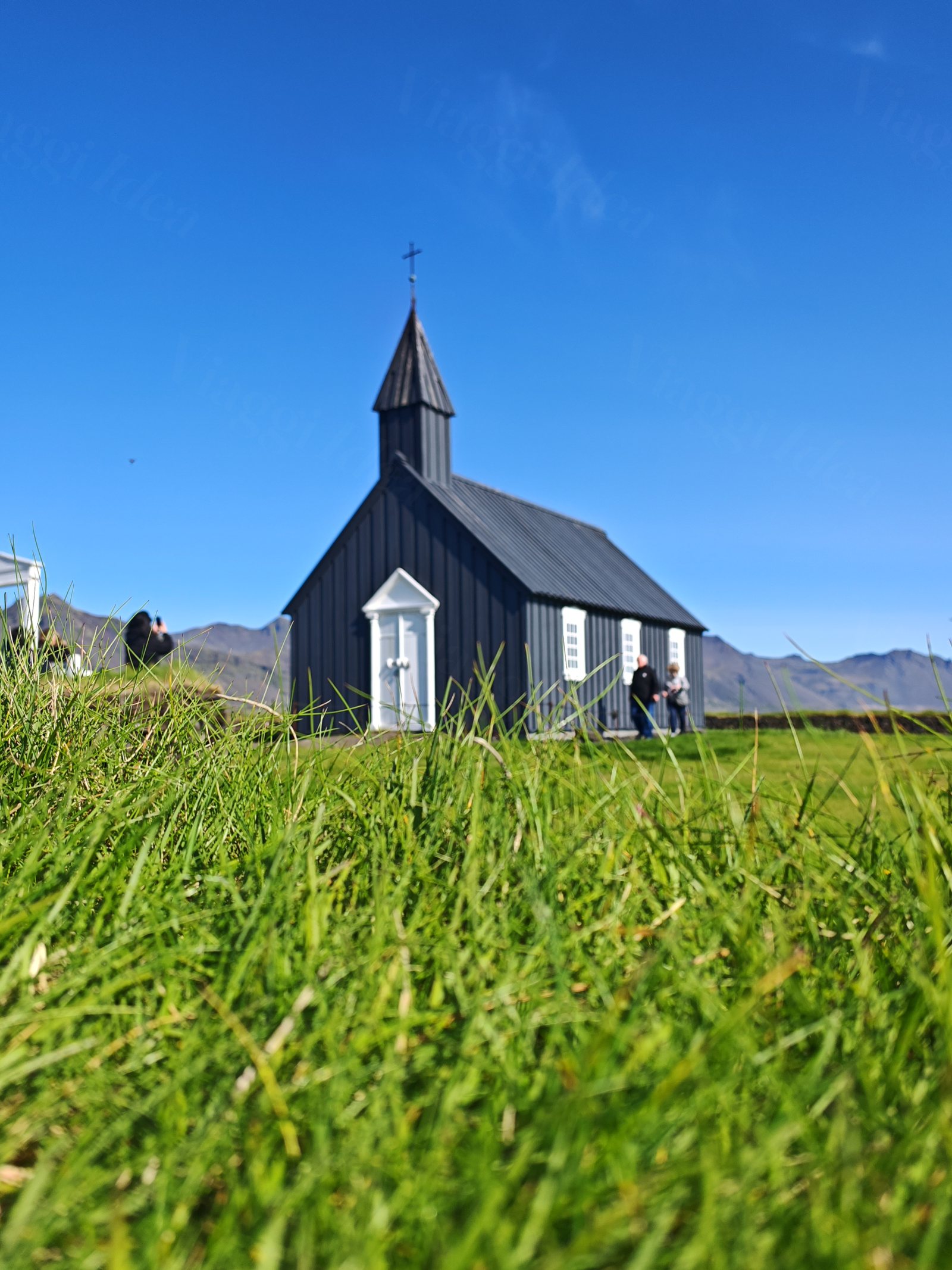 Persone vicino a una chiesa di legno nera con porta bianca in un campo verde