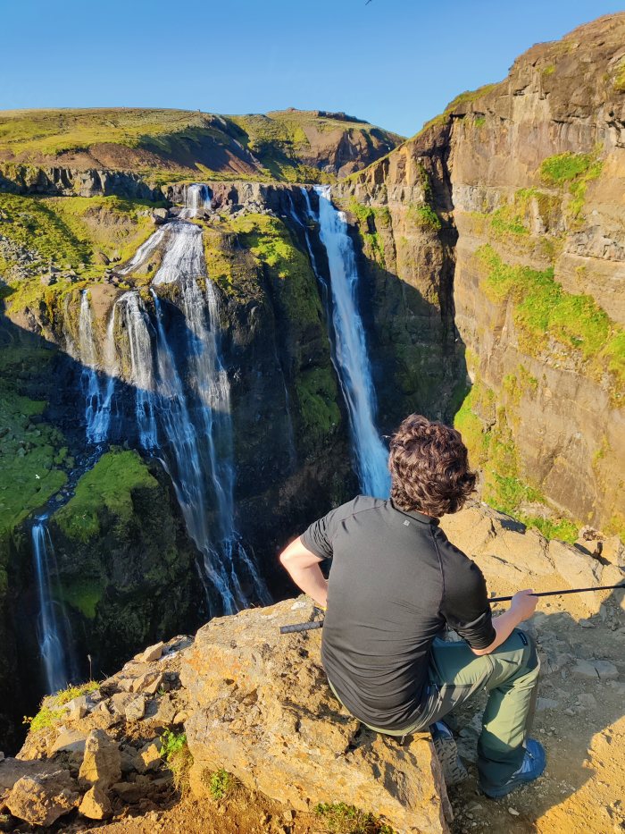 Un uomo seduto su una roccia guarda un imponente gruppo di cascate