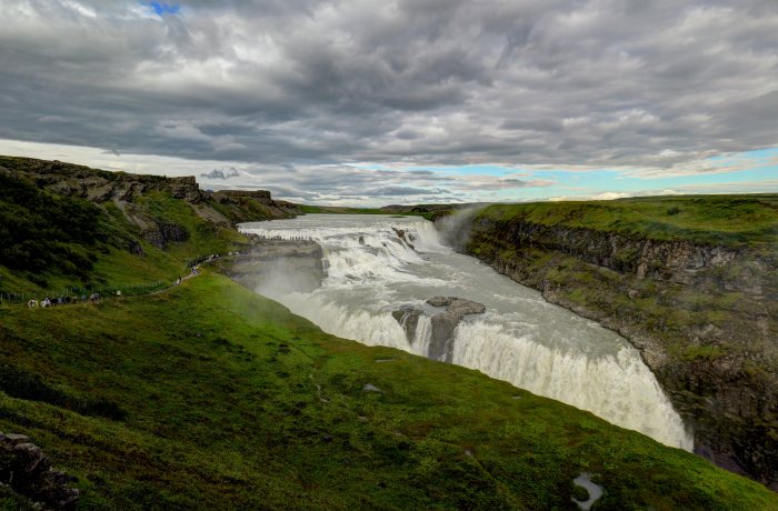 Gruppo di persone osserva un grande salto d'acqua fra colline verdi