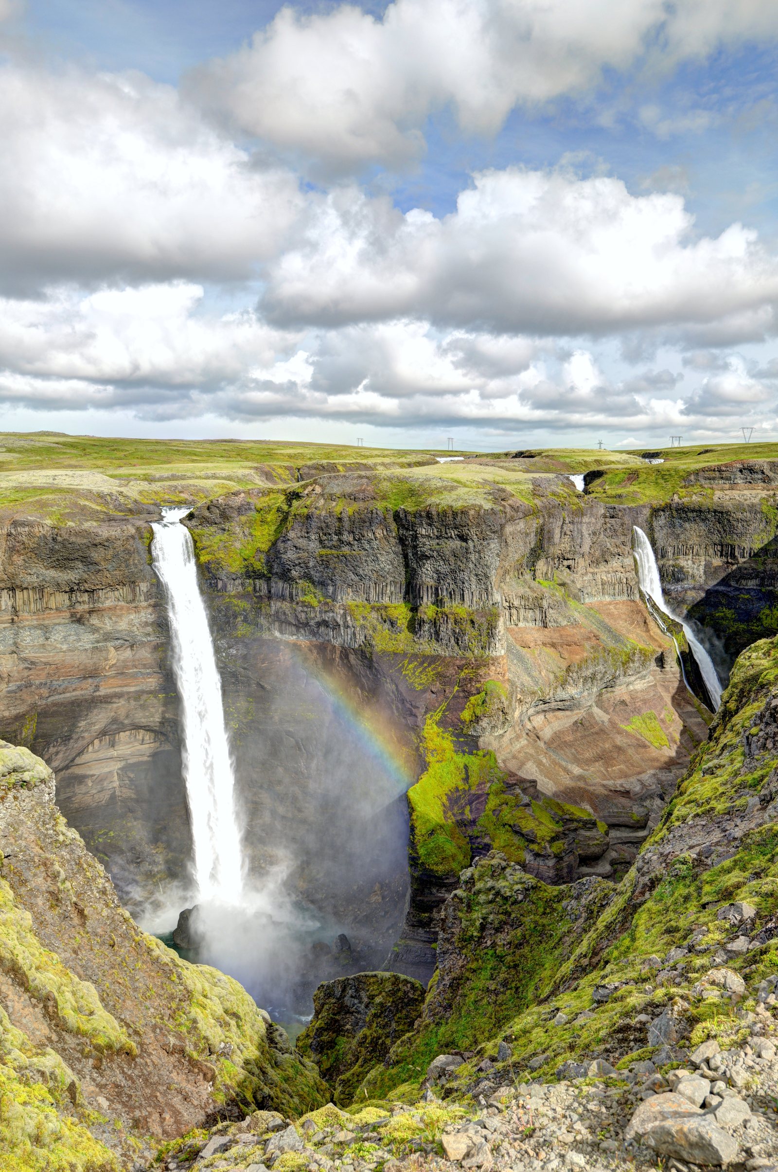 Cascata altissima dentro un canyon stretto con un arcobaleno sospeso nel vapore
