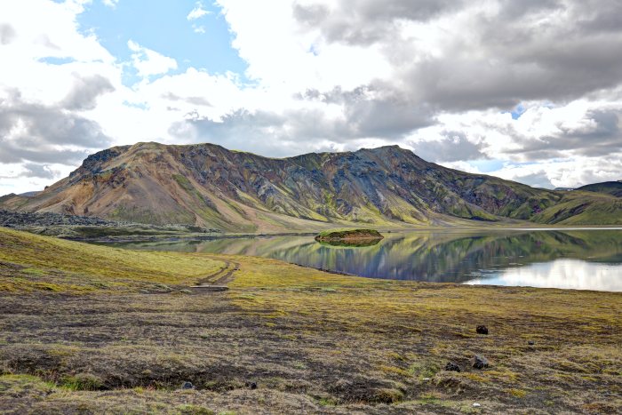 Lago scuro che riflette il versante vulcanico e le nuvole