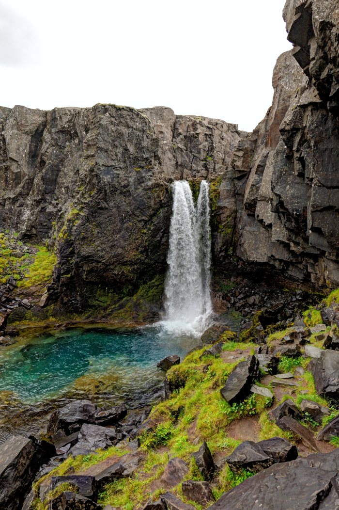 Acqua che cade in una pozza verde fra rocce e muschi