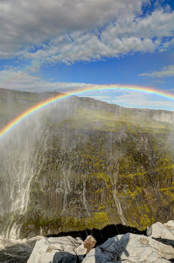 Un visitatore osserva un grande salto d'acqua con un arcobaleno sopra