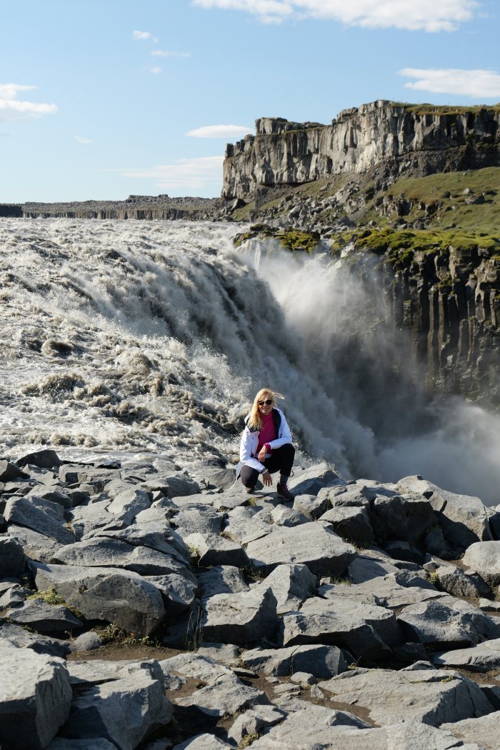 Una donna inginocchiata sulle rocce accanto a un grande salto d'acqua