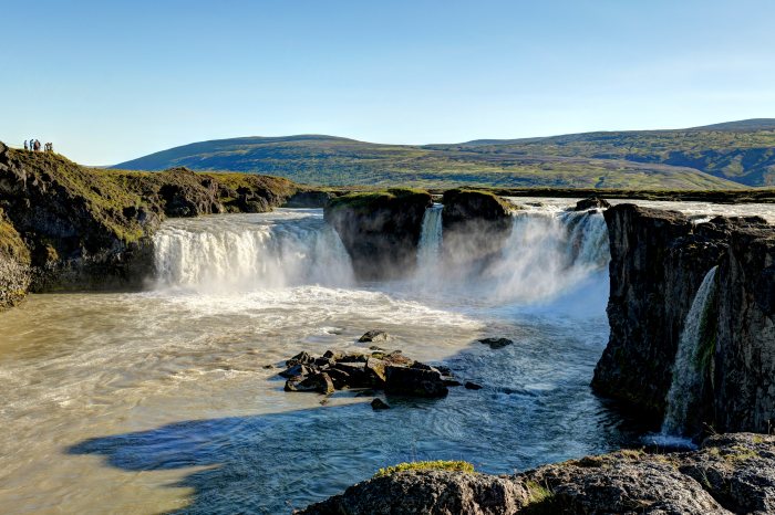 Gruppo di persone osserva un imponente salto d'acqua fra rocce e colline verdi