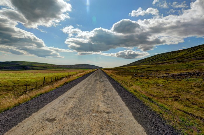 Strada sterrata che si estende fra campi e colline sotto un cielo nuvoloso