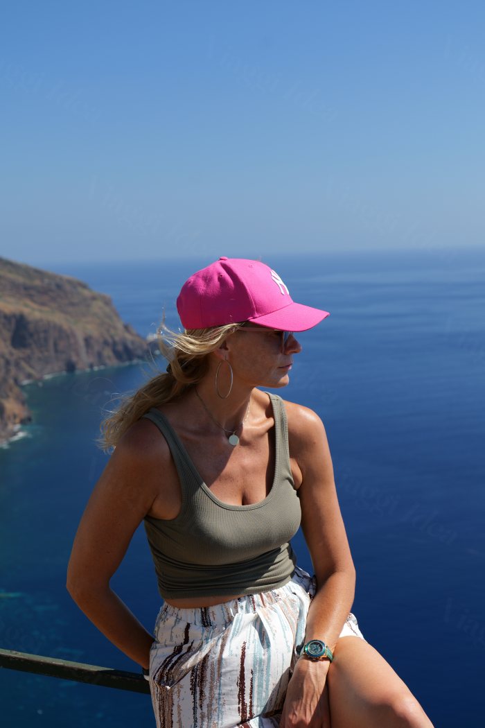Donna con cappello rosa che guarda il mare da un affaccio in alto sulla costa